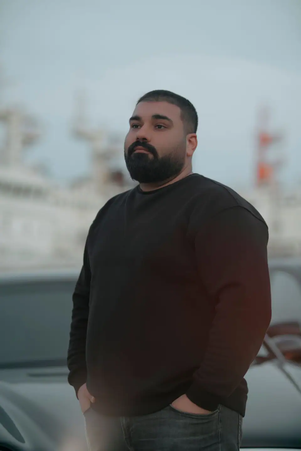A bearded man in a black sweatshirt by a harbor