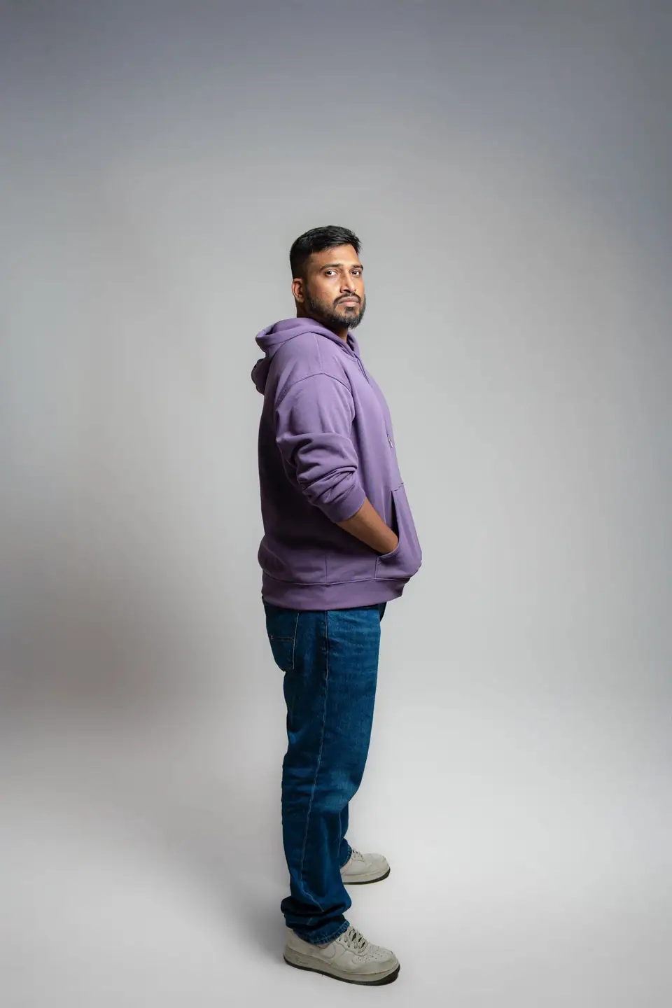 A man in a purple hoodie and jeans in a white studio