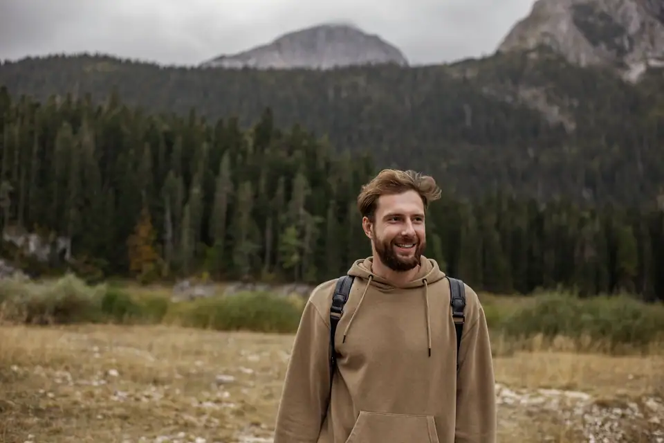 A smiling man in a tan hoodie on a mountain walk