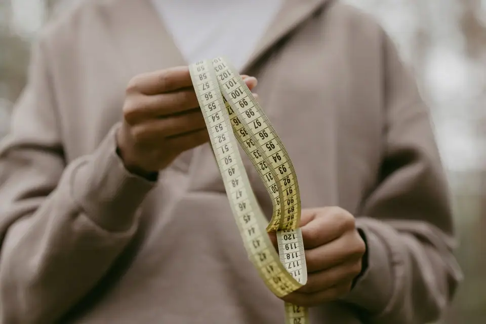 Hands holding a tape measure in front of a taupe hoodie