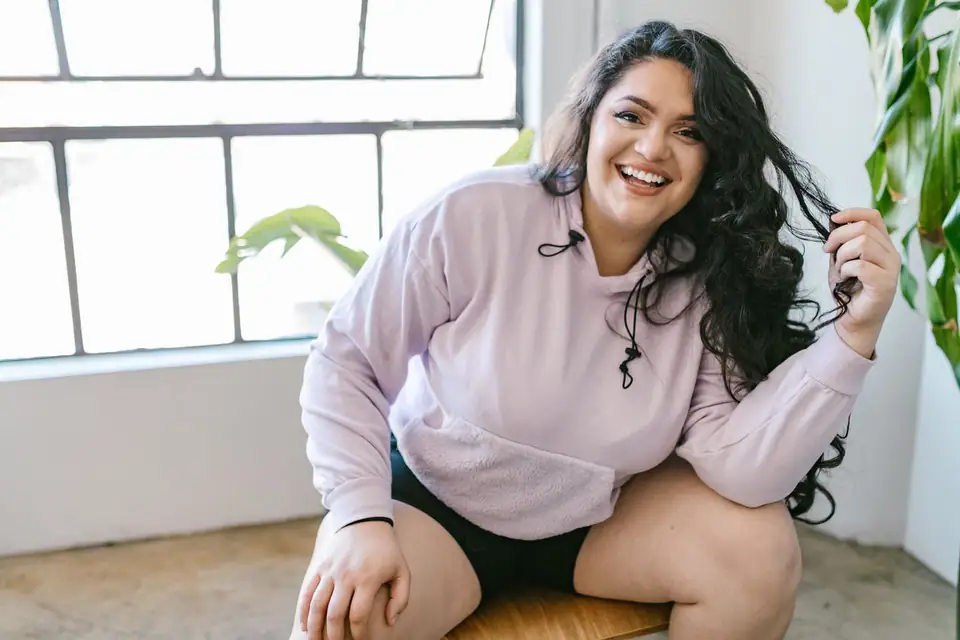 A smiling woman in a lilac cropped hoodie by a window